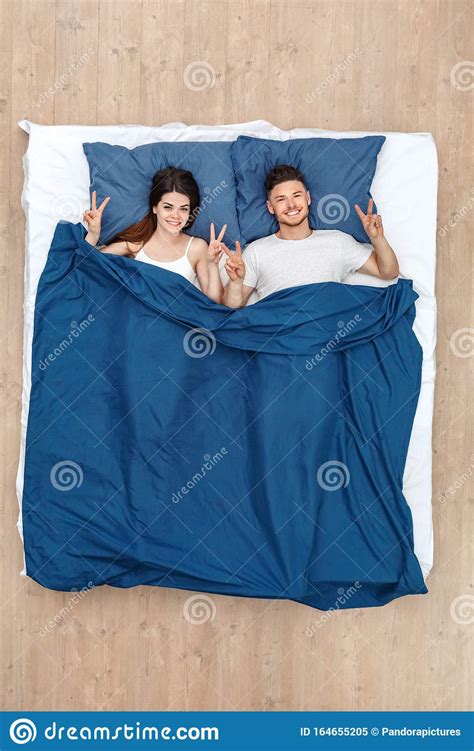 Bedtime Young Couple Lying On Bed Under Blanket Top View Posing Showing Salute Gesture Smiling