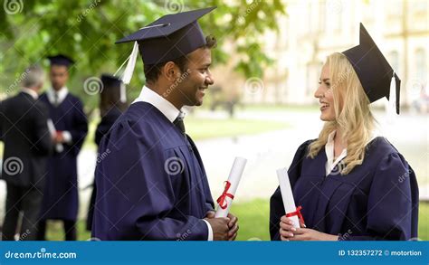 Couple Of Graduate Students With Diplomas Talking And Smiling To Each