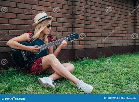 Pretty Long Haired Blonde Girl Sitting On Green Grass And Playing
