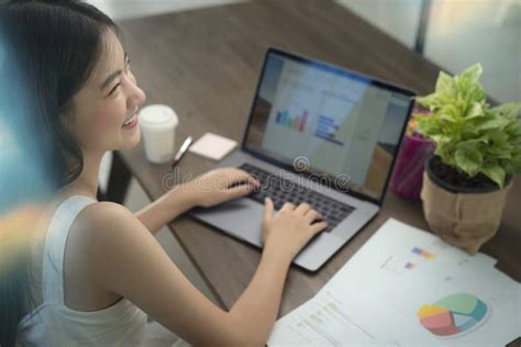 Asian Girl Typing Data To Her Computer Notebook For Prepare Her Report On The Wooden Deak Stock
