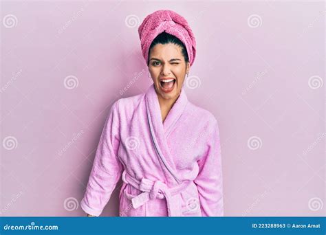 Young Hispanic Woman Wearing Shower Towel Cap And Bathrobe Winking