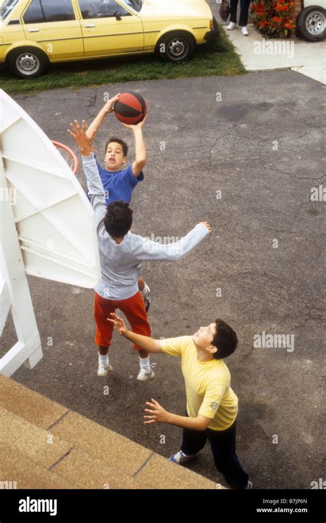 Three Boys Play Basketball On Driveway With Hoop Mounted On Roof Stock