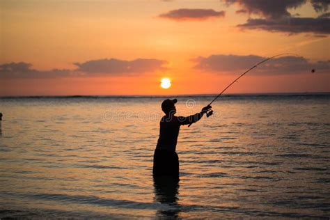 A Man Fishing In The Indian Ocean With The Beach At Sunset Stock Photo