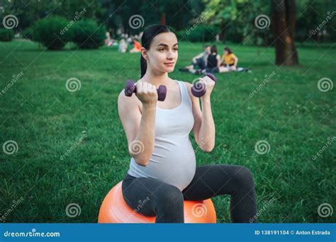 Young Fit Pregnant Woman Sit On Orange Fintess Ball In Park She