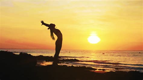 Silhouette Of Young Woman Is Doing Yoga Exercises On The Ocean Beach At