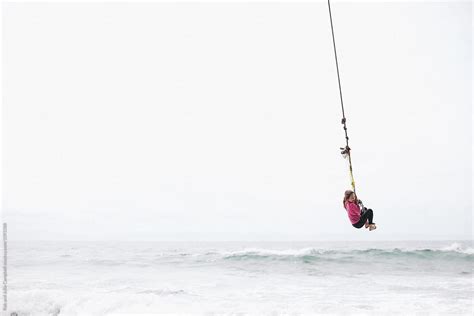 Young Girl Flying Over Ocean Water On Rope Swing Del Colaborador De