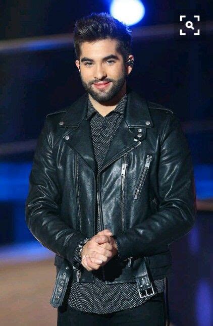 A Man Wearing A Black Leather Jacket Standing In Front Of A Blue Light And Smiling At The Camera