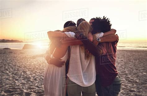 Young Friends Hugging In A Huddle On Sunset Summer Beach Stock Photo
