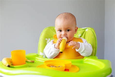 Baby Girl Eats Quinoa Porridge And Banana While Sitting On High Chair