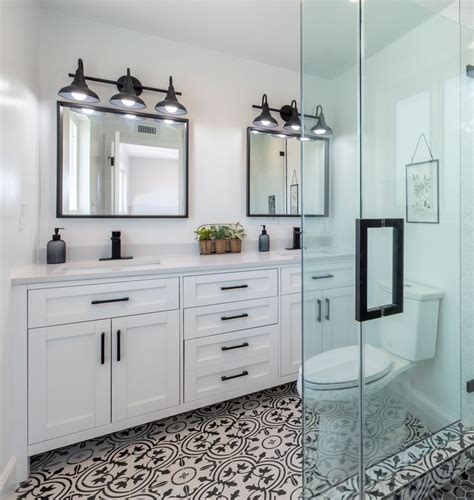 A White Bathroom With Black And White Tile Flooring Two Mirrors On The