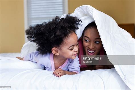Mother And Daughter Playing On Bed Hiding Under Duvet High Res Stock