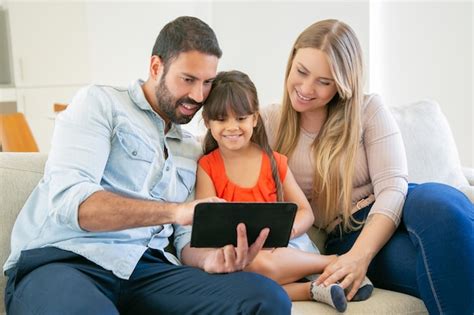 Padres Felices Y Linda Hija Sentada En El Sofá Usando Tableta Para