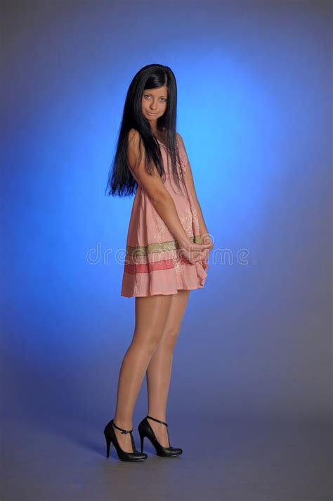 Brunette Girl In A Short Pink Dress On A Blue Background In The Studio