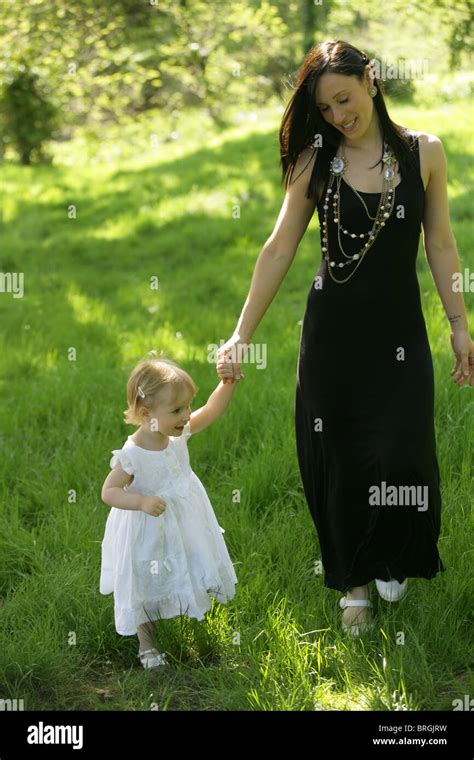 Mother And Daughter Walking Through Lush Grass Holding Hands Stock