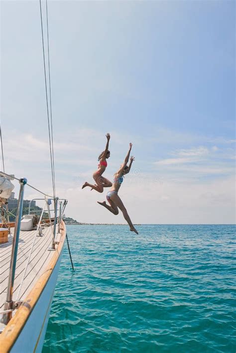Two Excited Friends Jumping Off A Boat Into The Ocean To Swim During