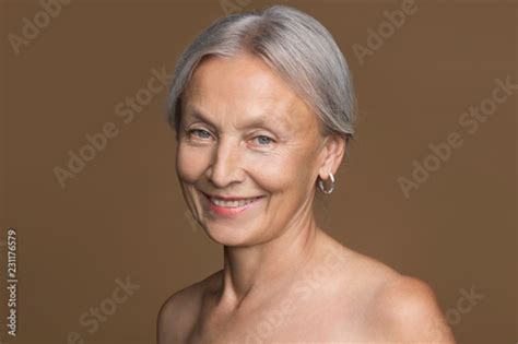 Portrait Of Naked Senior Woman With Grey Hair In Front Of Brown