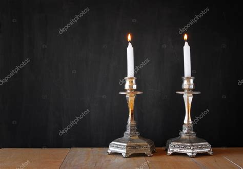 Two Candlesticks With Burning Candels Over Wooden Table And Blackboard