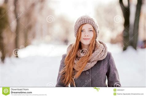 winter closeup portrait of a cute redhead lady in grey coat and scarf posing in the park stock