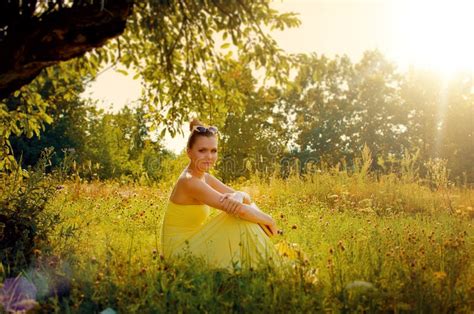 Beautiful Slim Woman In Yellow Dress Sitting On The Grass In The Stock