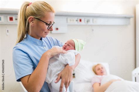 Young Nurse Standing In Maternity Ward And Holding Newborn Baby In Her