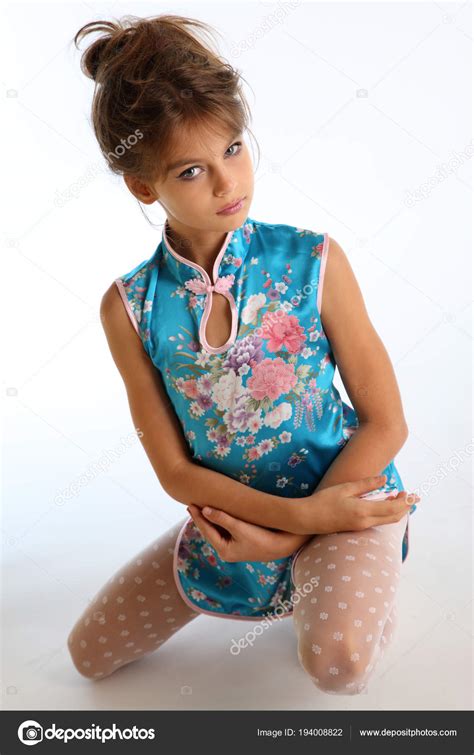 アジアの青いドレスの美しい少女は 白い背景に座っています スレンダーな身体と白ストッキングの長い脚を持つエレガントな魅力的な子 若いモデル