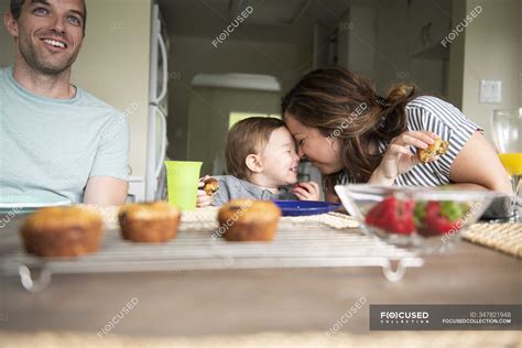 Happy Mother And Daughter Rubbing Noses At Kitchen Table Parenting