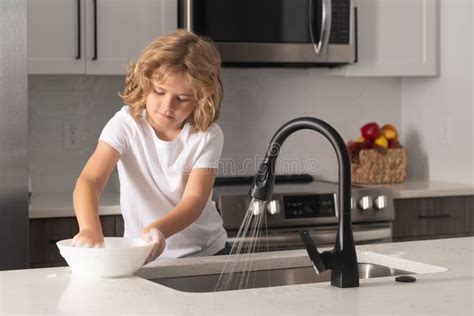 Child With Sponge With Dish Washing Liquid Is Doing The Dishes At Home