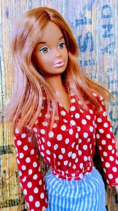 A Doll With Long Blonde Hair Wearing A Red Shirt And Blue Striped Skirt