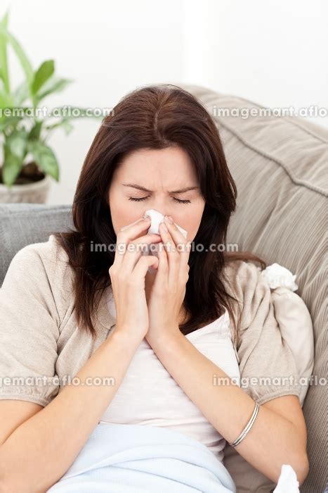 Portrait Of A Sick Woman Blowing Her Nose While Sitting On The Sofa At