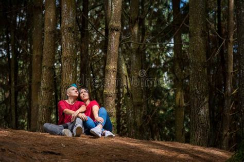 Lesbian Couple Sitting In The Woods Under A Tree With Sunlight On Them