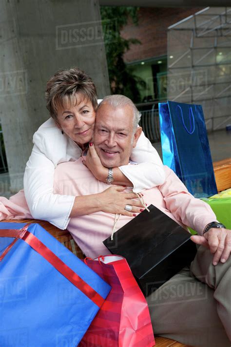 Senior Hispanic Woman Hugging Husband Surrounded By Ts Stock Photo