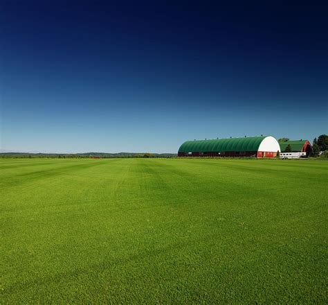 Sod Farm Field Of Grass Under Dark Blue Sky With Large Barns In