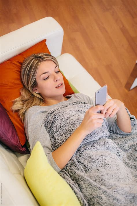 Cute Blonde Young Woman Using A Mobile Phone While Resting On A Couch
