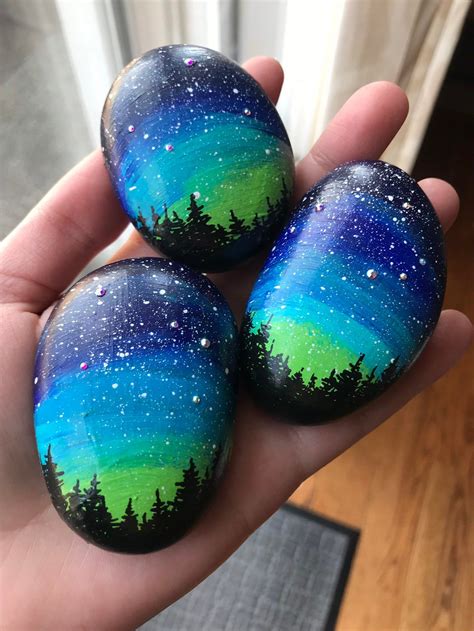 Three Painted Rocks In The Palm Of Someones Hand With Trees And Stars