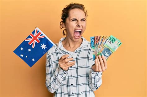 Young Brunette Woman Holding Australian Flag And Dollars Angry And Mad Screaming Frustrated And