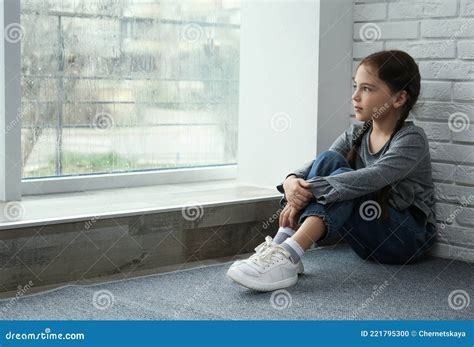 Sad Little Girl Sitting On Floor Near Window Space For Text Stock