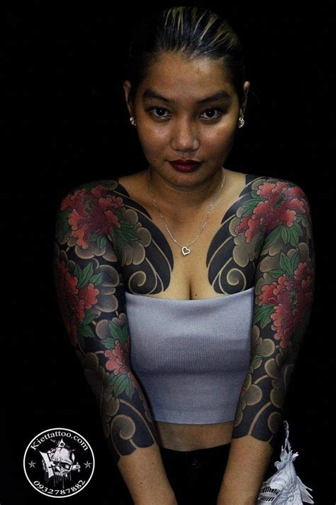 A Woman With Tattoos On Her Arms And Chest Is Posing For The Camera In Front Of A Black Background
