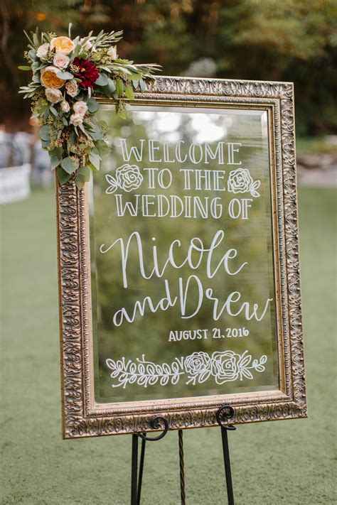 A Welcome Sign With Flowers On It In Front Of An Outdoor Ceremony Area