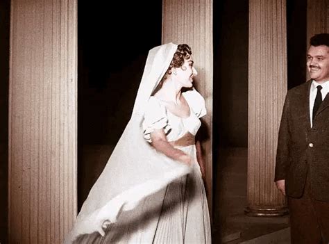 A Man And Woman Standing Next To Each Other In Front Of Pillars Wearing Wedding Dresses