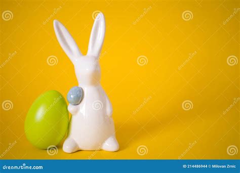 White Easter Bunny With Green Egg On Yellow Background Stock Photo