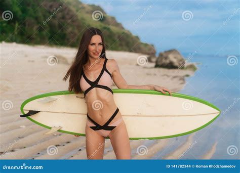 Beautiful Brunette Girl In Swimsuit Goes On Sandy Beach With Surfboard