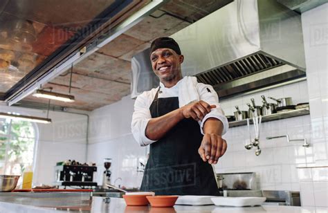Happy Male Cook Wearing Apron Standing By Kitchen Counter And Smiling Gourmet Chef In Uniform