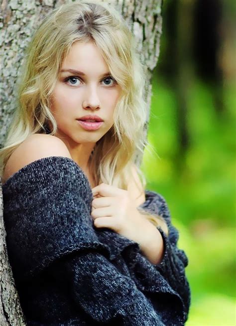 a beautiful blond woman leaning against a tree