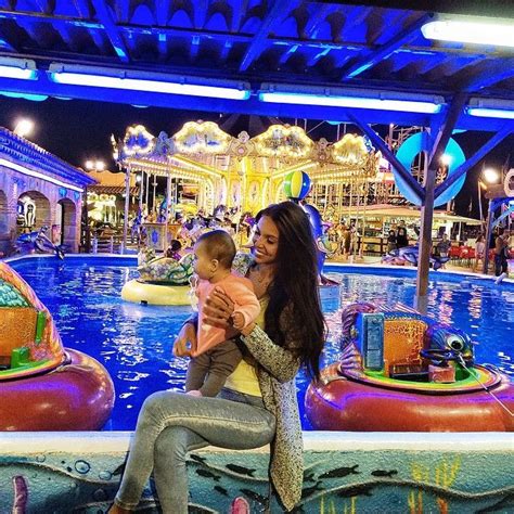 A Woman Holding A Baby In Front Of An Amusement Park Ride Area At Night