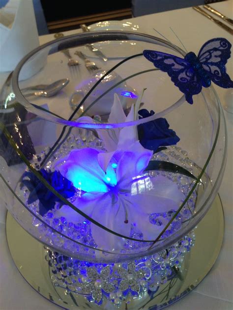 A Glass Bowl Filled With Flowers And Butterflies On Top Of A White