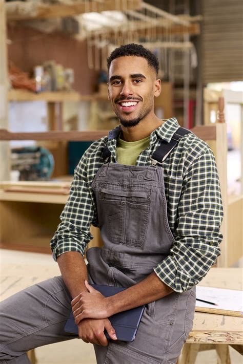 Portrait Of Male Apprentice Working As Carpenter In Furniture Workshop