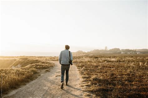Young Man Walking Down Path Through A Field On Coast By Stocksy