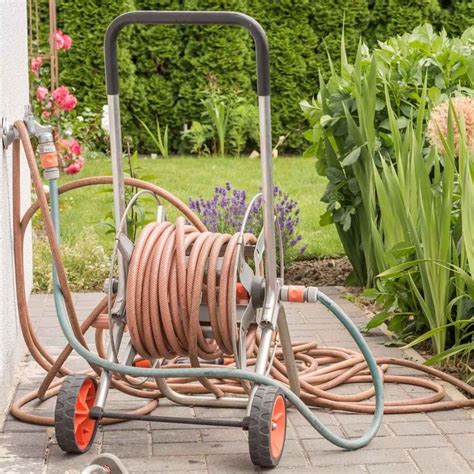 A Garden Hose Cart With Two Hoses Attached To It And Flowers In The Background