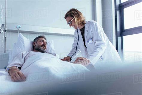 hospitalized man lying in bed while doctor checking his pulse female physician examining male