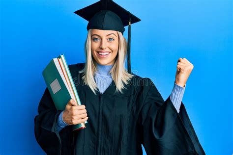 Beautiful Blonde Woman Wearing Graduation Cap And Ceremony Robe Holding